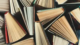 Photo shows several books crammed together, some are partially open.