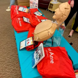 Picture of one CPR mannequin inflated sitting on a table, with five other red kits laid around it.