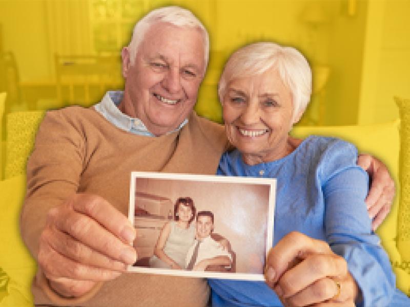 an elderly couple holding an old photo of them as a younger couple