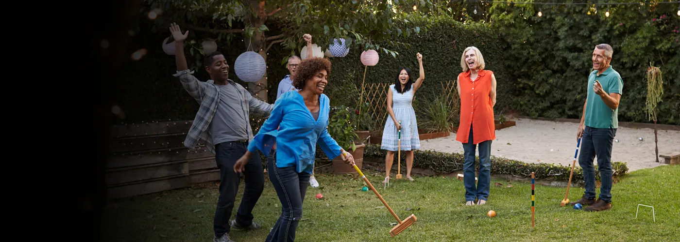 adults playing croquet in a grass backyard. 