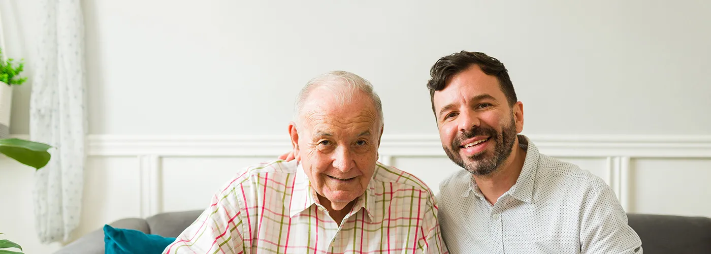 an elderly man with his adult son sitting on a couch smiling