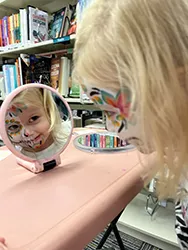 Photo of a child looking in a small mirror wearing face paint