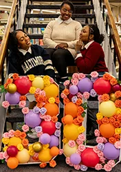 Group of 3 women sitting on steps, posing by the number 30 made out of balloons